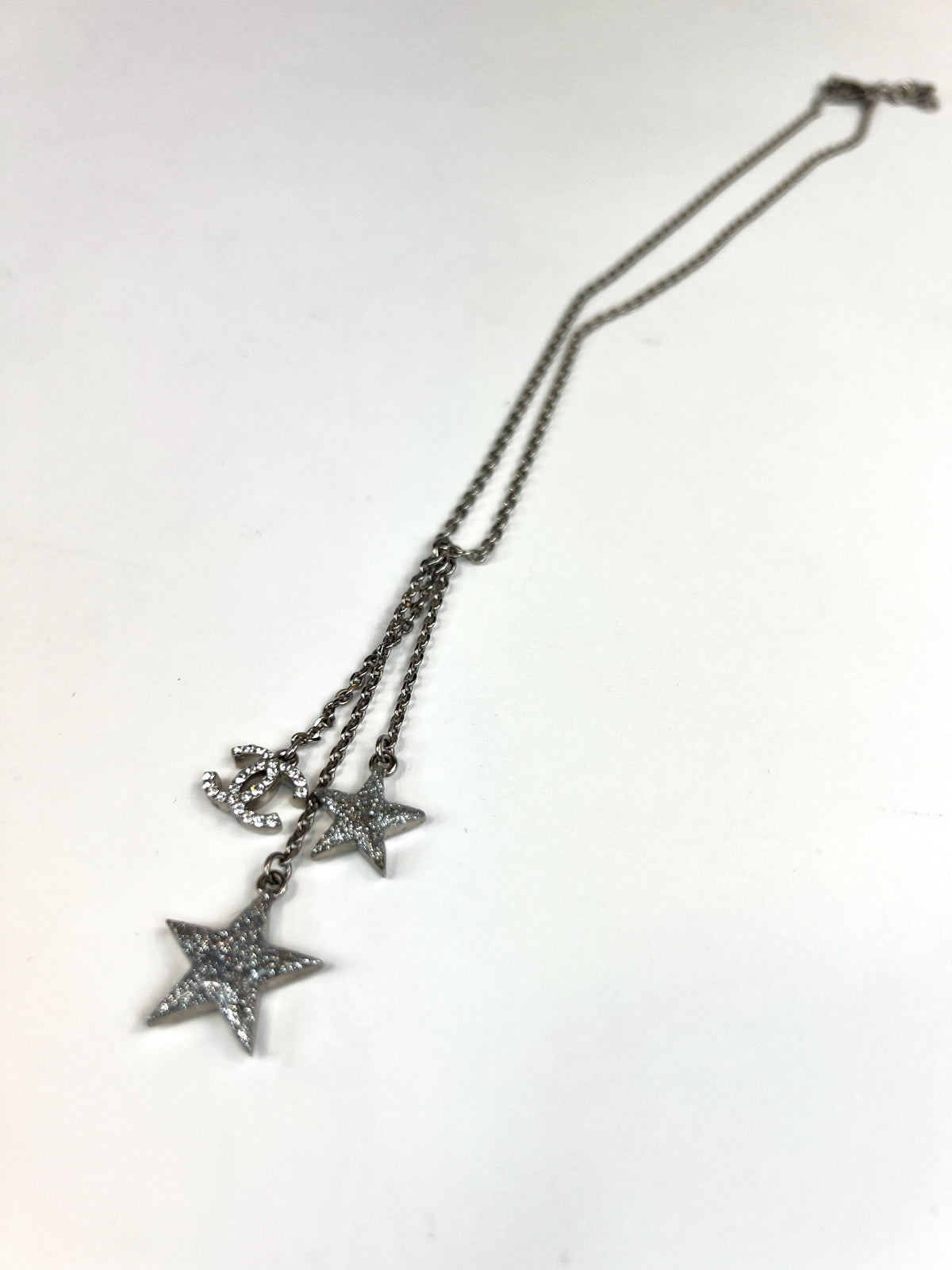 Excellent Pre-Loved Silver Toned Crystal Embellished 2 Star Motif and Logo Pendant Drop Necklace.  (flat lay)